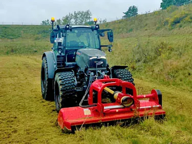 Traktor mit Mulchgerät beim Mähen einer großen Grünfläche